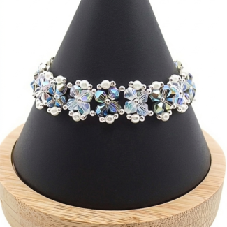 Handmade bracelet featuring iridescent opal and silvery grey aurora borealis AB finish faceted crystals and small white pearls woven together in a repeating floral cluster pattern with silver-tone bead accents, shown worn on a black mannequin hand and wrist against a white background.