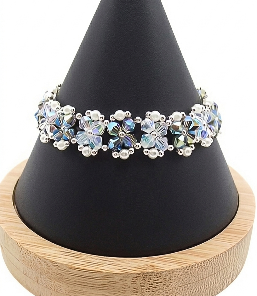 Handmade bracelet featuring iridescent opal and silvery grey aurora borealis AB finish faceted crystals and small white pearls woven together in a repeating floral cluster pattern with silver-tone bead accents, shown worn on a black mannequin hand and wrist against a white background.