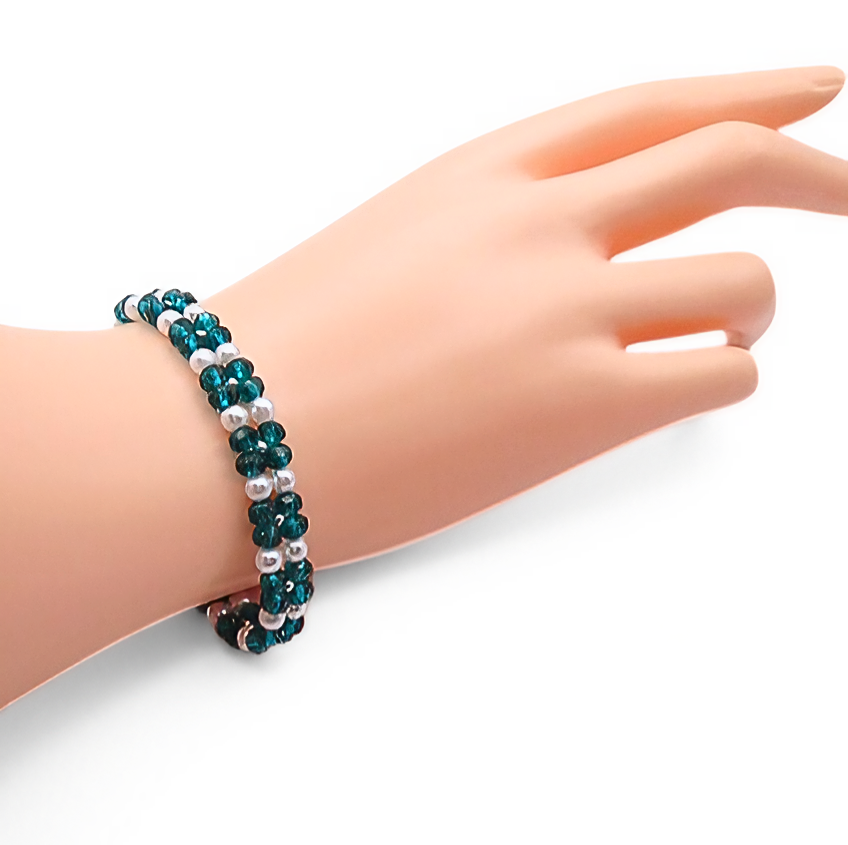 Handmade teal crystal and white pearl floral bracelet featuring repeating four-petal crystal flower motifs with pearl centres and silver seed bead accents, with a silver-tone lobster clasp, shown worn on a mannequin wrist and hand against a white background.