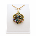 Iridescent crystal pendant necklace with gold-coloured chain and bail, displayed on a white jewellery stand, showcasing multi-colored metallic beadwork design