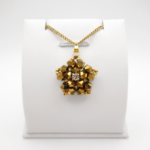 Intricate gold-coloured crystal pendant featuring faceted crystals arranged in a star-pattern with gold accents and a sparkling cubic zirconia centre, shown against a white display stand.