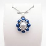 Blue and white pearl pendant necklace with silver beadwork detailing and a matching silver-tone chain displayed on a white jewellery stand.