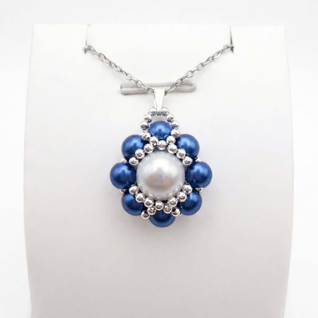 blue-pearl-pendant-display Blue and white pearl pendant necklace with silver beadwork detailing and a matching silver-tone chain displayed on a white jewellery stand.