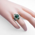 Emerald green crystal ring with white pearl beading worn on hand mannequin, close-up view