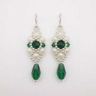 Handcrafted drop earrings made with deep emerald green crystals, white pearl beads, and silver accents hanging against a neutral background.