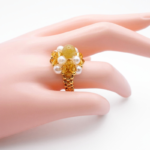 Handmade cocktail ring featuring golden crystals, white pearls, and a gold-toned tourmaline stone displayed on a mannequin hand model.