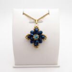 Navy blue crystal pendant with metallic blue crystals, aquamarine-coloured centre crystal, gold-coloured bead accents and matching chain. Shown on a display stand.