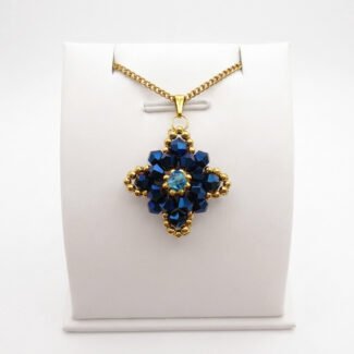 Navy blue crystal pendant with metallic blue crystals, aquamarine-coloured centre crystal, gold-coloured bead accents and matching chain. Shown on a display stand.