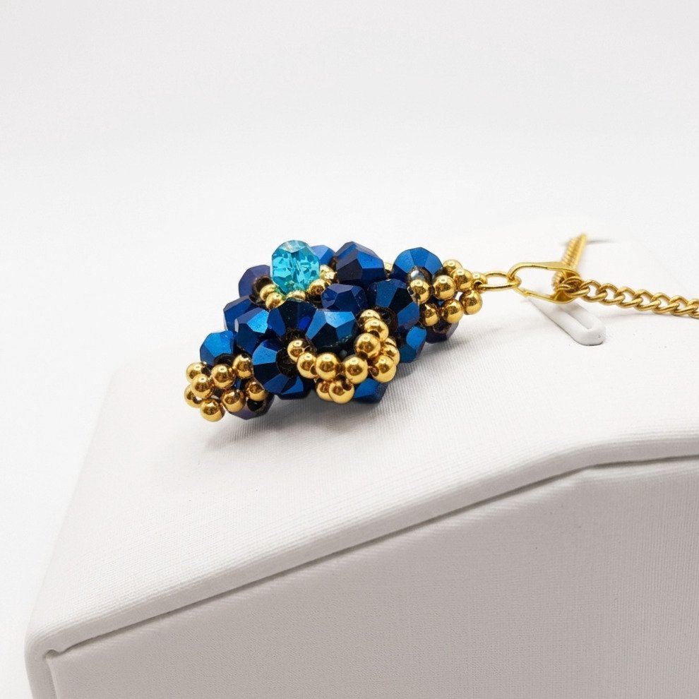 navy-blue-crystal-pendant-side-view Side view of the navy blue crystal pendant with metallic blue crystals, aquamarine-coloured centre crystal, gold-coloured bead accents and matching chain. Shown on a display stand.