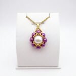 Purple and white pearl pendant necklace with gold beadwork detailing and a matching gold-tone chain displayed on a white jewellery stand.
