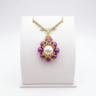 Purple and white pearl pendant necklace with gold beadwork detailing and a matching gold-tone chain displayed on a white jewellery stand.