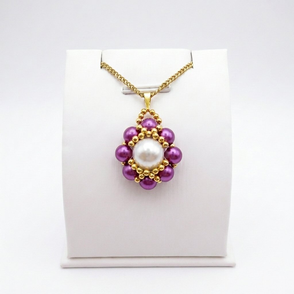 purple-pearl-pendant-display Purple and white pearl pendant necklace with gold beadwork detailing and a matching gold-tone chain displayed on a white jewellery stand.