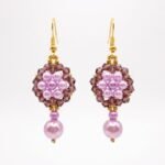 Pair of elegant purple pearl and crystal earrings with luminous lavender pearls, faceted plum-purple crystals, gold-coloured accents and dangling pearl drops on a neutral background.
