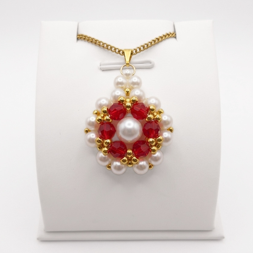 red-crystal-pearl-pendant-display Front view of flower-design pendant featuring off-white pearls and faceted red crystals. The pendant has a matching gold bail and a gold chain, shown on a display stand.