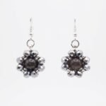 Dark grey tourmaline gemstone centre surrounded by shimmering metallic silver crystals and silver hooks, shown against a neutral background.