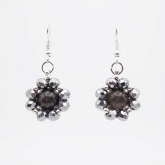 Dark grey tourmaline gemstone centre surrounded by shimmering metallic silver crystals and silver hooks, shown against a neutral background.
