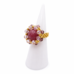 A side view of a purple tourmaline ring with pink and purple crystals and gold-tone beads on a white ring display cone.