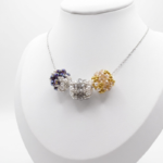 Three handmade crystal and pearl bead pendants in amethyst purple, smoke grey and champagne gold on a silver-tone chain, displayed on a white jewellery bust display stand.