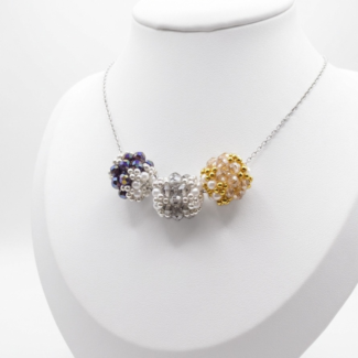 Three handmade crystal and pearl bead pendants in amethyst purple, smoke grey and champagne gold on a silver-tone chain, displayed on a white jewellery bust display stand.