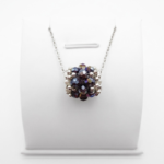 Handmade barrel-shaped amethyst AB crystal pendant necklace with white pearls and silver-tone beads on a silver chain, displayed on a white jewellery stand