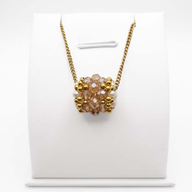 barrel-crystal-pendant-champagne Handmade barrel-shaped gold champagne crystal pendant necklace with white pearls and gold-tone beads on a gold chain, displayed on a white jewellery stand