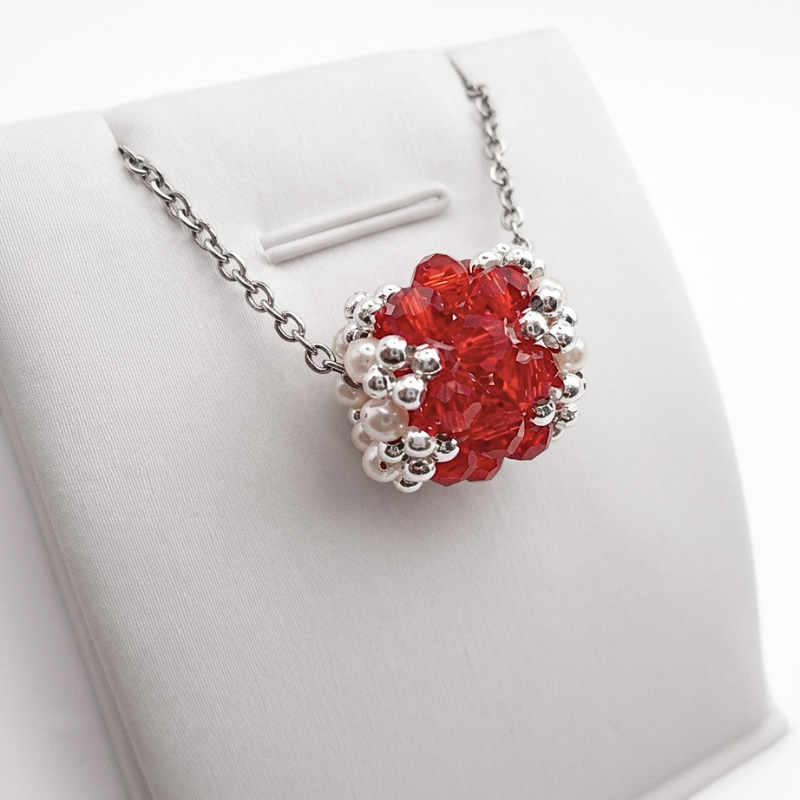 barrel-crystal-pendant-red Silver-tone chain necklace with an intricate woven beaded barrel-shaped pendant made of red crystals and white pearls, shown on a display stand against a white background.
