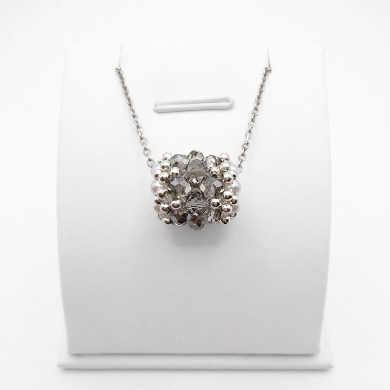 barrel-crystal-pendant-silver Handmade barrel-shaped silver-grey crystal pendant necklace with white pearls and silver-tone beads on a silver chain, displayed on a white jewellery stand