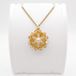 Handmade golden crystal flower pendant necklace with white pearl centre and gold-tone beads on a gold chain, displayed on a white jewellery stand