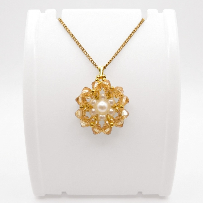 golden-crystal-pendant-front-view Handmade golden crystal flower pendant necklace with white pearl centre and gold-tone beads on a gold chain, displayed on a white jewellery stand