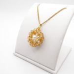 A side view of a golden crystal flower pendant with white pearl centre and gold-tone beads on a gold chain, displayed on a white jewellery stand