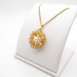 A side view of a golden crystal flower pendant with white pearl centre and gold-tone beads on a gold chain, displayed on a white jewellery stand