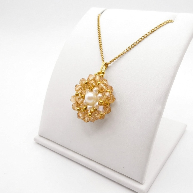 golden-crystal-pendant-side-view A side view of a golden crystal flower pendant with white pearl centre and gold-tone beads on a gold chain, displayed on a white jewellery stand