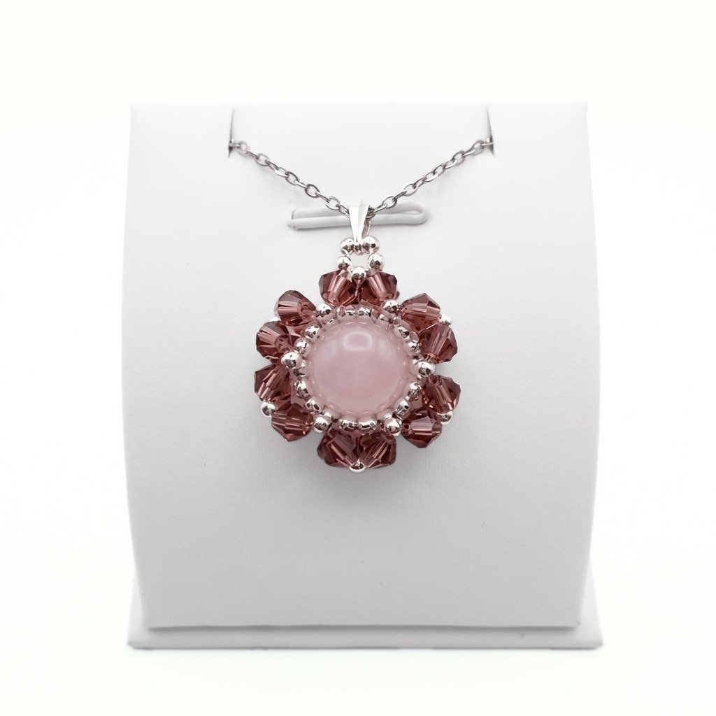 rose-quartz-flower-pendant-front-view Handmade rose quartz and purple crystal flower pendant necklace with silver-tone beads on a silver chain, displayed on a white jewellery stand